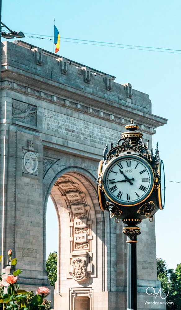 Arch of Triumph in Bucharest with a decorative clock in the foreground.