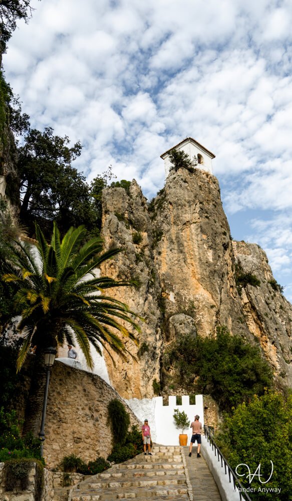 Iconic white bell tower of Guadalest rising above palm trees and cliffs.