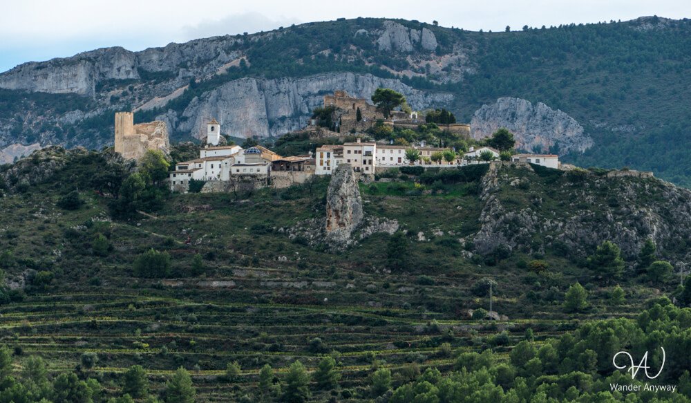 Distant view of Guadalest Castle and village nestled between mountains.
