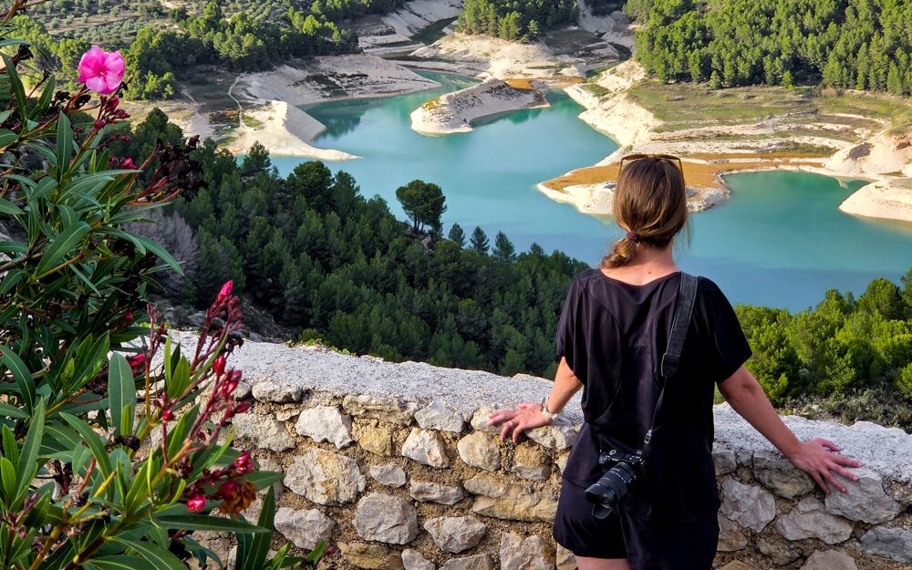 Traveler overlooking the turquoise Guadalest Reservoir from viewpoint.